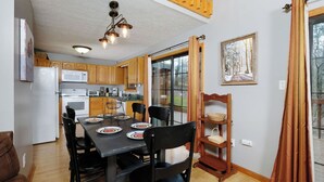 A modern kitchen with wooden cabinets, a dining table set for four, and a large window with a view of trees.
