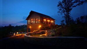 A wooden cabin with a glass upper level, surrounded by a stone retaining wall and a small waterfall. - Shooting Star - Stunning Views, Wi-Fi, Pool Table (Sevierville)