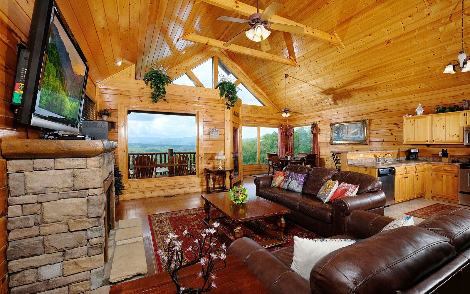 Un intérieur de chalet chaleureux avec une cheminée en pierre, des canapés en cuir, un coin repas et une cuisine.