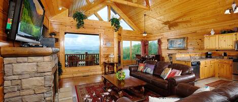Un intérieur de chalet chaleureux avec une cheminée en pierre, des canapés en cuir, un coin repas et une cuisine.