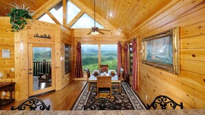 A wooden cabin with a dining area, a ceiling fan, and a large window offering a view of the forest. - Shooting Star - Stunning Views, Wi-Fi, Pool Table (Sevierville)