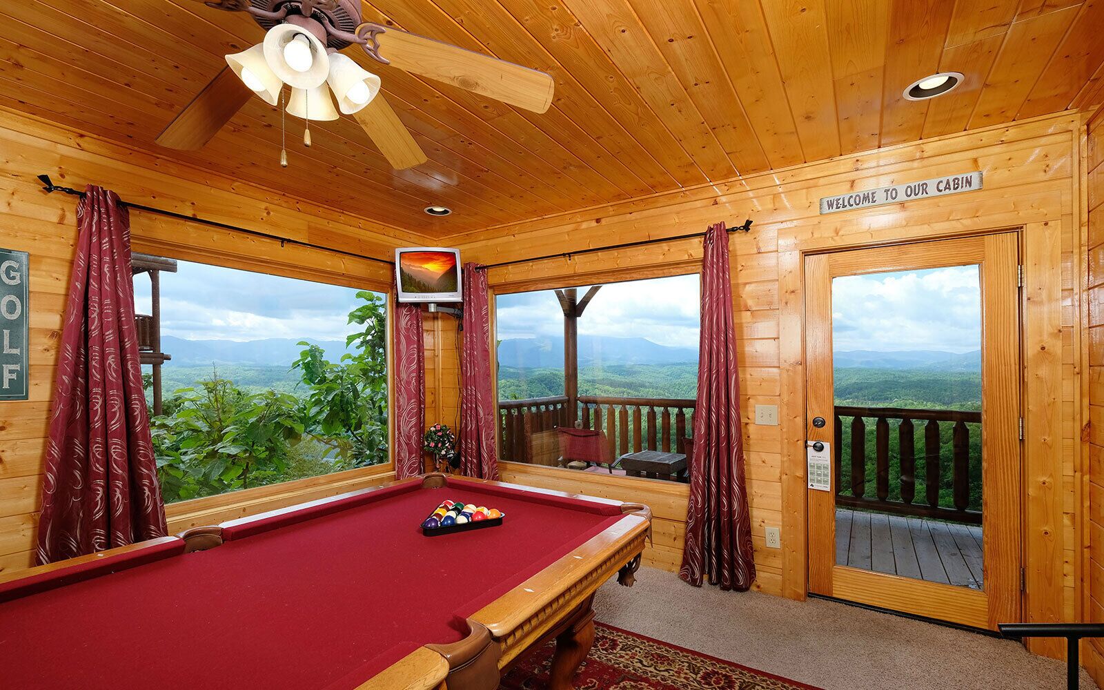 A cabin with a pool table, a ceiling fan, and a sign reading "Welcome to our cabin."