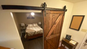 Ein Schlafzimmer mit einem Bett, Nachttischlampen, einer Holztür, einem kleinen Tisch mit einem Dankeschön-Schild und einem gerahmten Bild an der Wand.