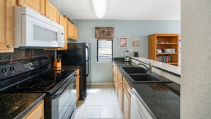 Una cocina moderna con armarios de madera, una estufa negra, un microondas blanco y un refrigerador negro.