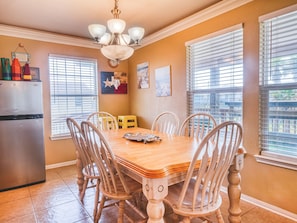 A dining area with a wooden table and chairs, a chandelier, and a refrigerator. - ‘Seas The Moment’….. before it passes you by. (Freeport)