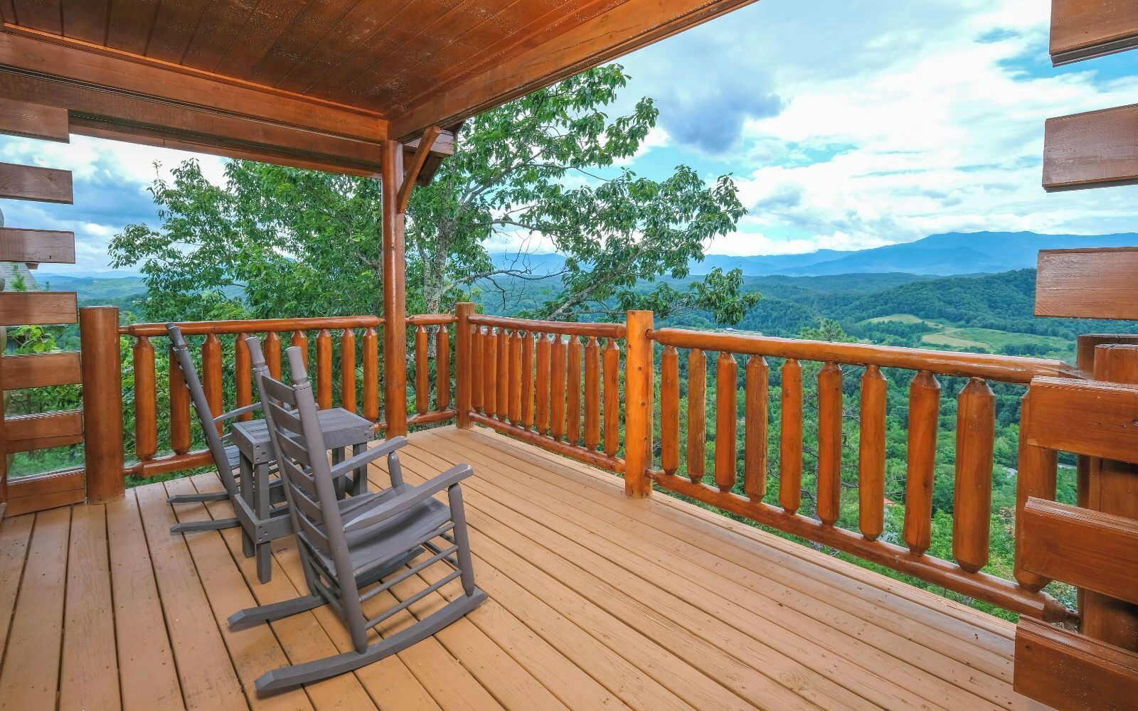 A wooden deck with a wooden railing, a table, and two chairs.