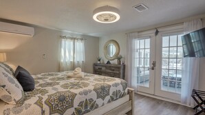 Een slaapkamer met een bed, een dressoir, een spiegel en een schuifdeur naar een balkon.