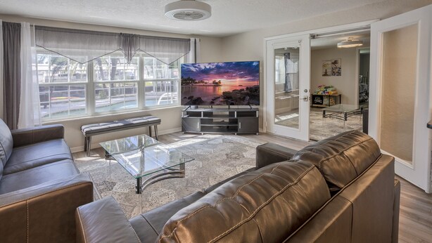 Een woonkamer met een leren bank, een glazen salontafel en een tv waarop een zonsondergang te zien is.