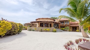 A resort with a sandy beach, a palm tree, and a building with a red roof.