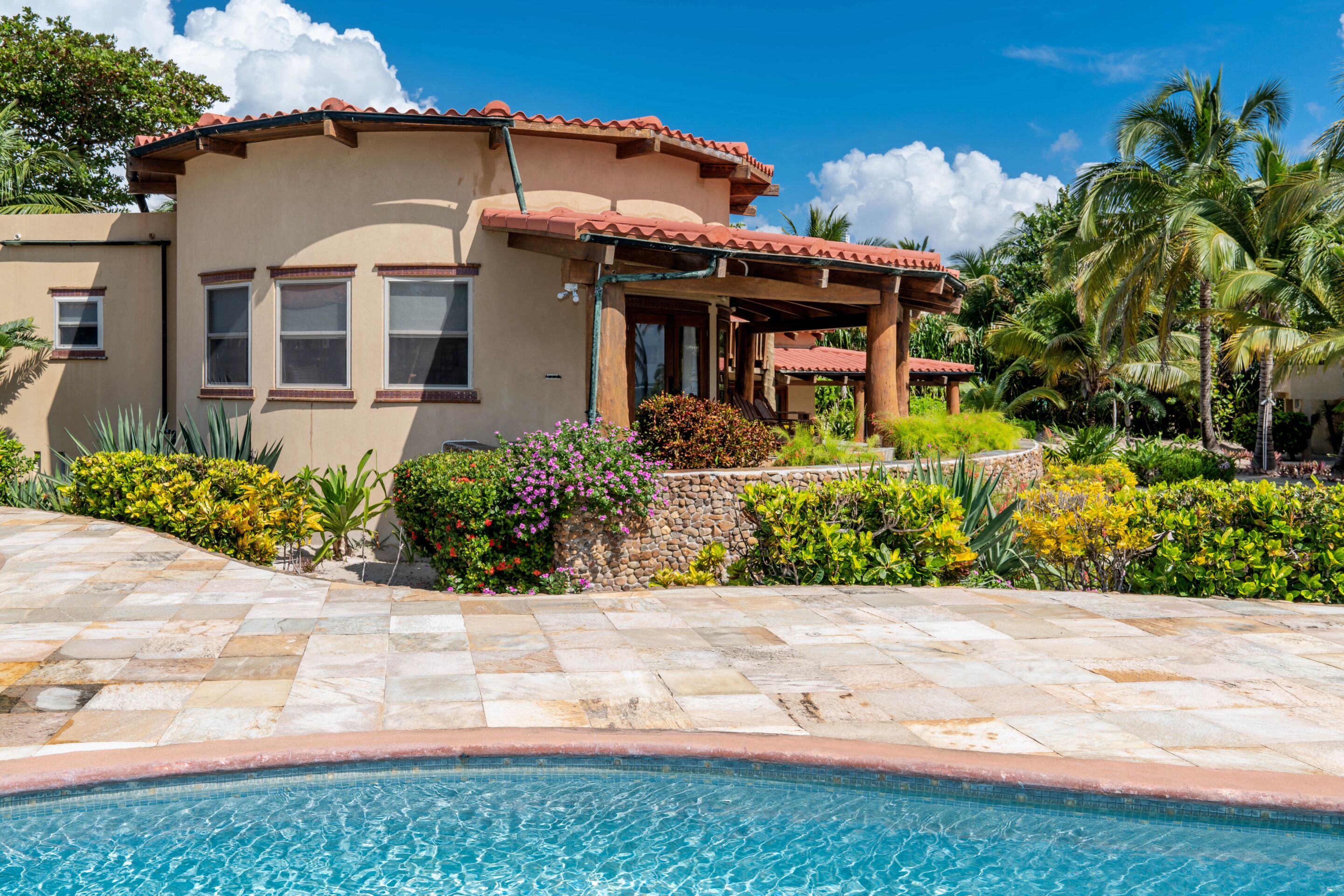 A house with a swimming pool, surrounded by tropical plants and palm trees.