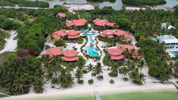 An aerial view of a resort with multiple red-roofed buildings, a central swimming pool, and a beach area. - Luxury Villa In A Private Beachfront Oasis, W/ Tennis, Pickleball, Dock/ Pool! (San Pedro)