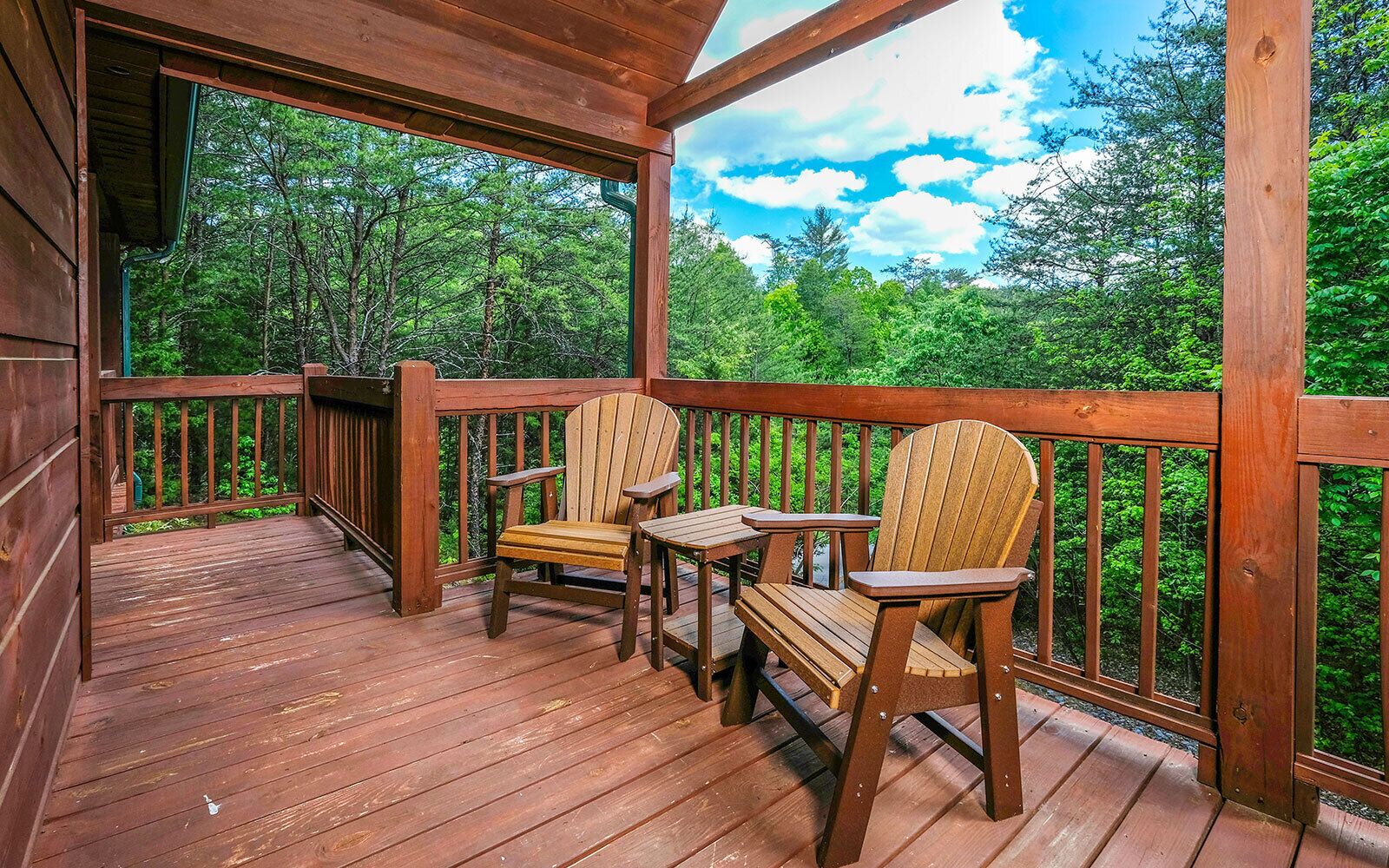 A wooden deck with two Adirondack chairs and a small table, surrounded by a wooden railing.