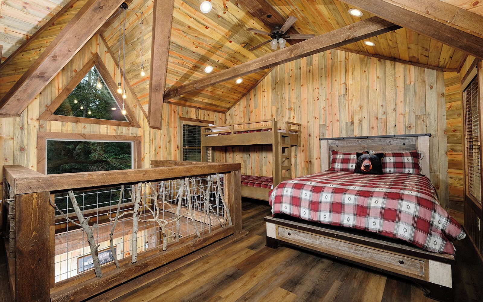 Une chambre dans une cabane en bois, avec un lit superposé, une fenêtre donnant sur les arbres et un ventilateur de plafond.