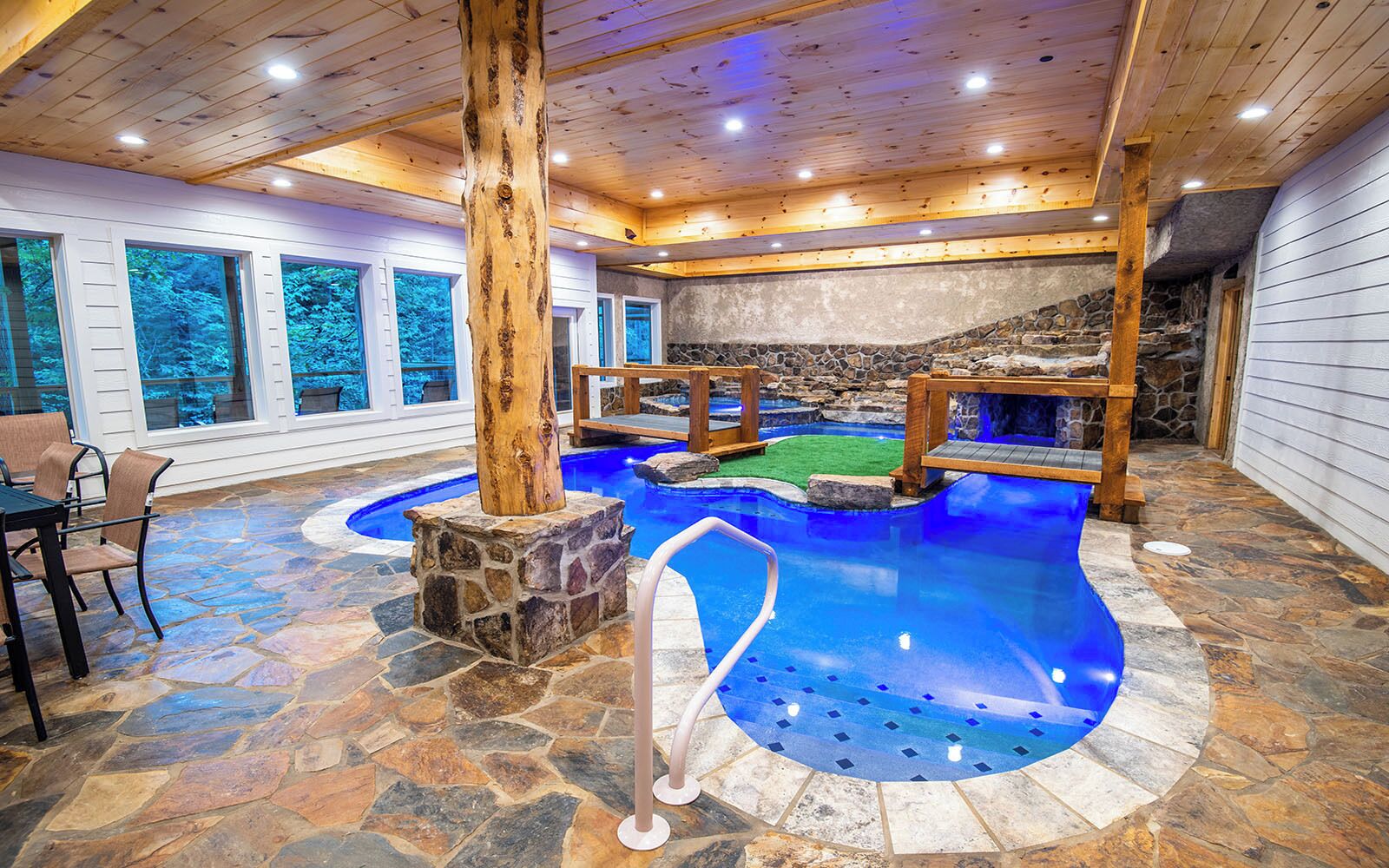 An indoor swimming pool with stone flooring, wooden beams, and a stone wall backdrop.