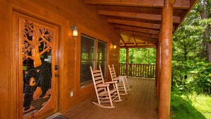 A wooden cabin with a porch, rocking chairs, and a large tree carving on the door. - 🐻Can't Bear to Leave: Theater, Two King Suites, Games, Fireplaces & Hot Tub🌄 (Pigeon Forge)