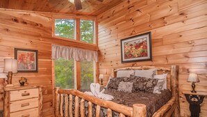 A wooden cabin bedroom with a bed, dresser, and two windows. - 🐻Can't Bear to Leave: Theater, Two King Suites, Games, Fireplaces & Hot Tub🌄 (Pigeon Forge)