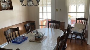 A dining room with a round table, wooden chairs, a chandelier, and a window with lace curtains.