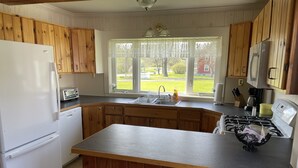 A kitchen with wooden cabinets, a white refrigerator, a sink, a stove, and a window with a view of the outdoors.