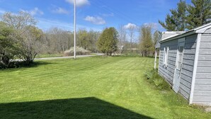 A grassy yard with a wooden building, trees, and a clear sky.