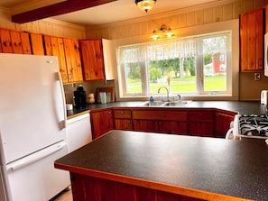 A kitchen with wooden cabinets, a refrigerator, a sink, and a window with a view of the outdoors.