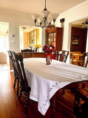 A dining room with a large table, chairs, a chandelier, and a vase with flowers.