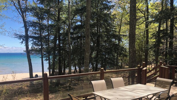 Una terraza de madera con una mesa y sillas, con vistas a una playa y un bosque.