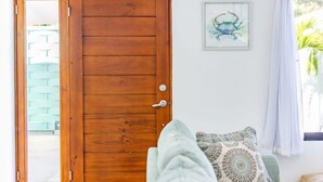 A wooden door with a view of a building outside, a framed picture on the wall, and a window with curtains.