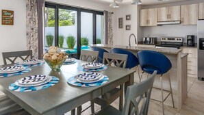 A modern kitchen with a central island, a dining area with blue chairs, and a view of greenery outside.