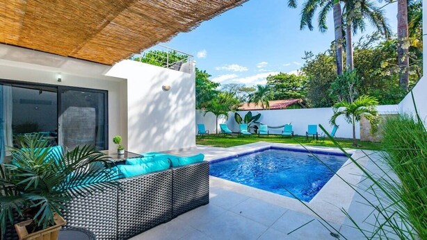 A modern outdoor pool area with a built-in seating area and a thatched roof.
