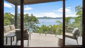 A balcony with a sofa and chairs, overlooking a lake and mountains. - 5-BD Beachfront, Ocean-View Hillside Home (Playa Flamingo)