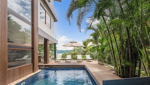 A modern pool area with a clear view of the pool, lounge chairs, and a wooden deck. - 5-BD Beachfront, Ocean-View Hillside Home (Playa Flamingo)