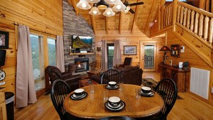 A cozy cabin interior with a dining table set for four, a fireplace, and a staircase leading to an upper level. - Still Life - Mountain Views and Hot Tub (Sevierville)