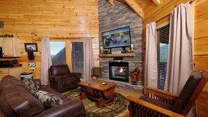 A cozy cabin interior with a stone fireplace, leather furniture, and a television mounted on the wall. - Still Life - Mountain Views and Hot Tub (Sevierville)