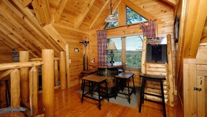 A log cabin interior with a wooden dining table, chairs, a lamp, and a window with curtains. - Still Life - Mountain Views and Hot Tub (Sevierville)