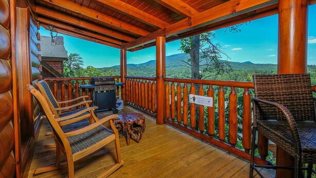 A covered porch with wooden chairs, a grill, and a view of a mountainous landscape. - Still Life - Mountain Views and Hot Tub (Sevierville)