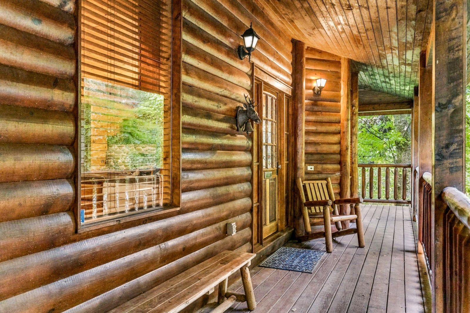 Una cabaña de troncos con un porche, bancos de madera y vistas al bosque circundante.