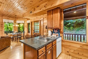 Interior de una cabaña de madera con cocina, comedor y vistas al exterior.