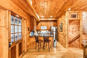 Interior de una cabaña de madera con cocina, comedor y escalera.