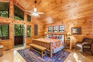 Un dormitorio de cabaña de madera con cama, banco, silla y ventilador de techo.