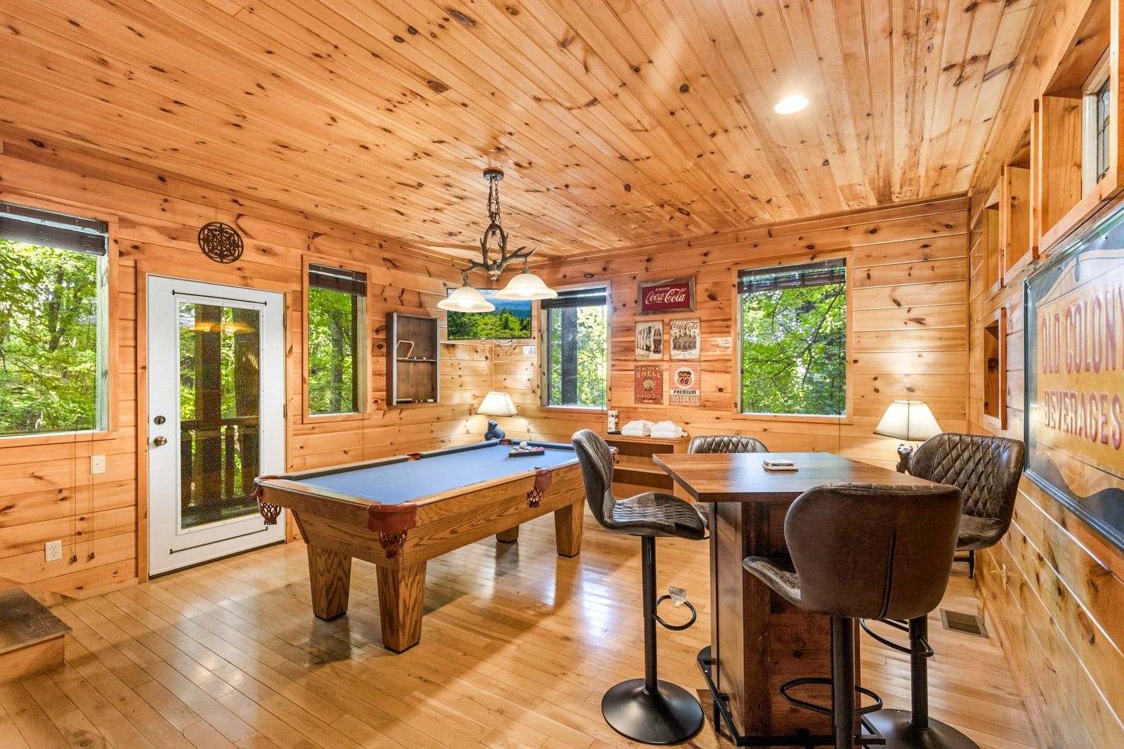 A wooden interior with a pool table, bar stools, and a Coca-Cola sign.