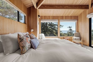 A bedroom with a large bed, a chair, and a view of the outdoors.