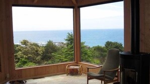 Una habitación con un ventanal grande con vista al mar, una chimenea y una zona de estar con sofá y sillones.
