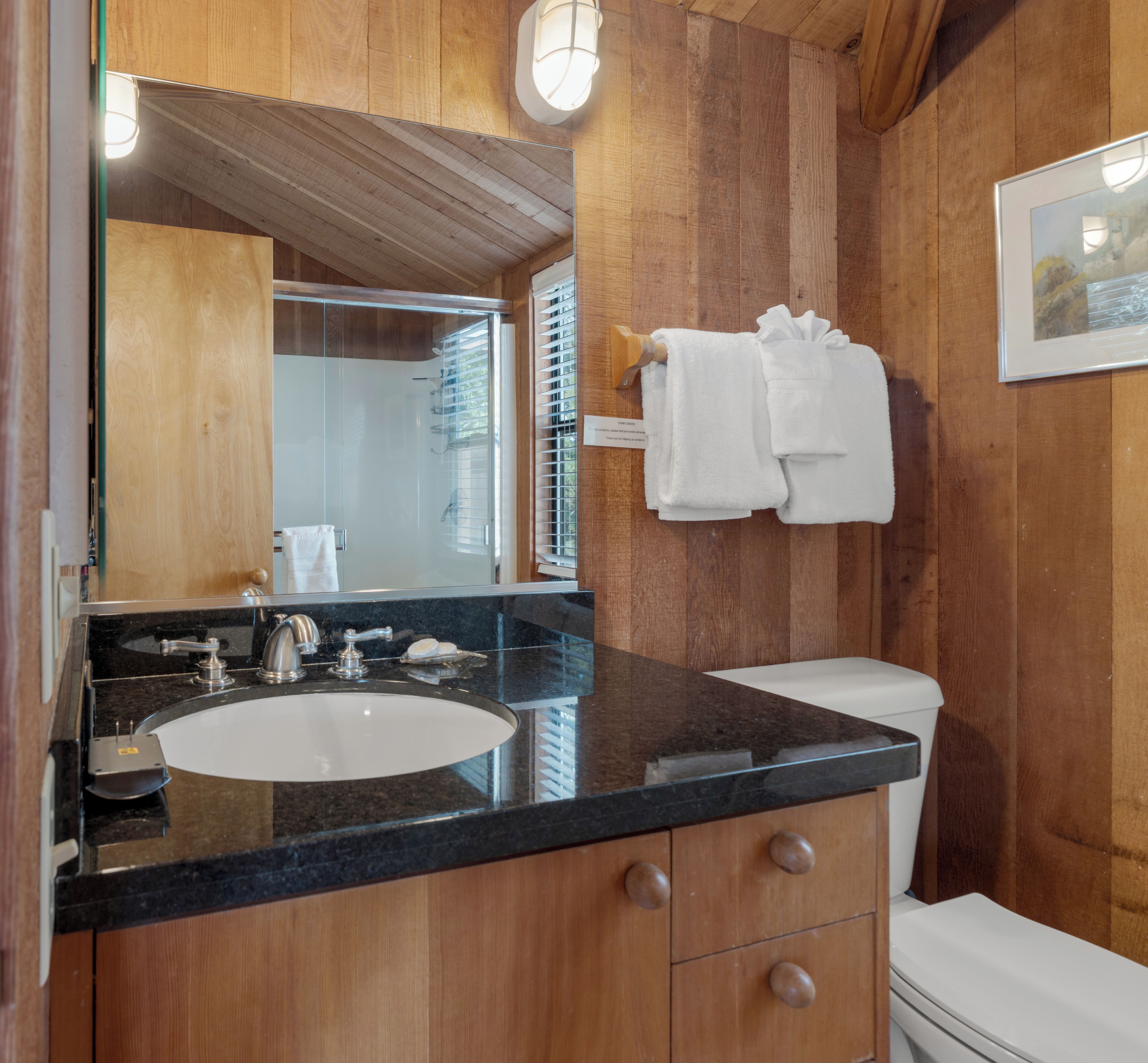A bathroom with a wooden interior, a sink with a mirror, a toilet, and a towel rack.