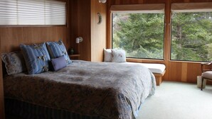 Un dormitorio con una cama grande, un banco, una ventana y vistas a árboles.