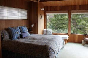 Una camera da letto con un letto grande, una panca, una finestra e vista su alberi.