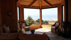 Una habitación acogedora con techo de madera, un ventanal con vistas a un paisaje, chimenea y asientos cómodos.