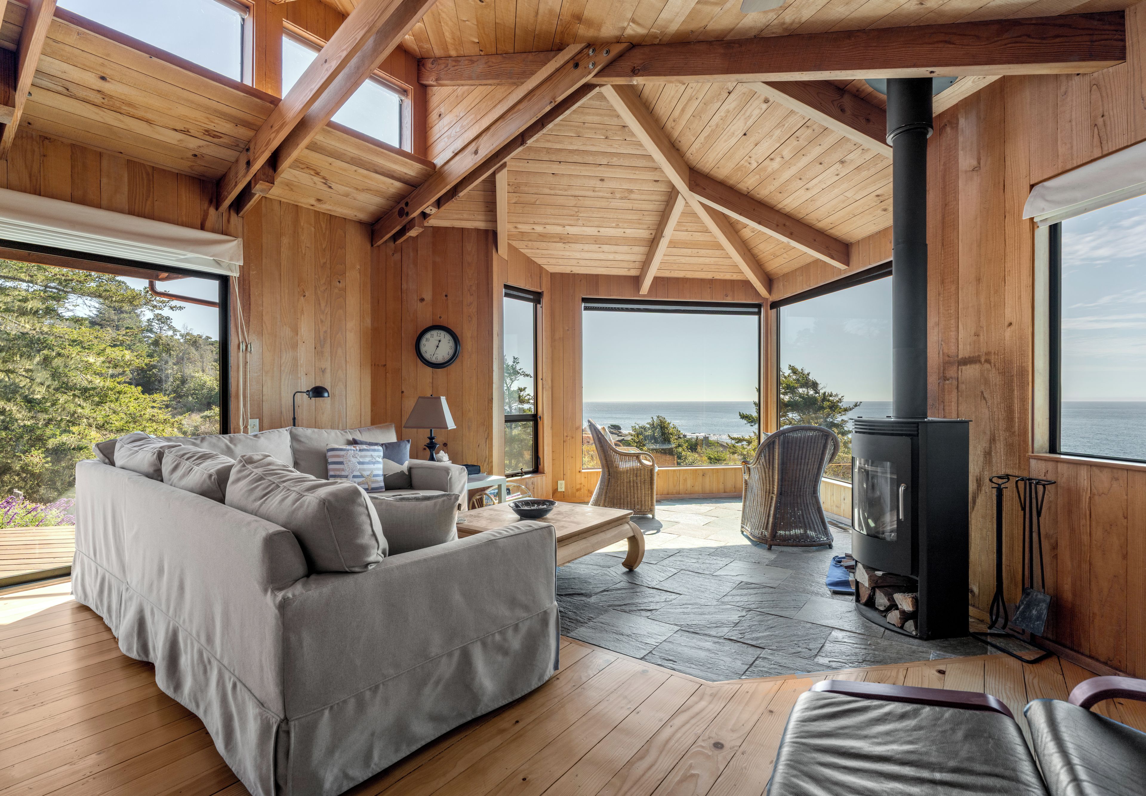 A spacious living area with a wooden ceiling, large windows, a sofa, a table, and a fireplace.