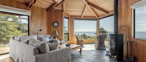 A spacious living area with a wooden ceiling, large windows, a sofa, a table, and a fireplace.