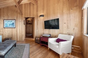 A wooden interior with a white armchair, a flat-screen TV mounted on the wall, and a framed picture on the wall.