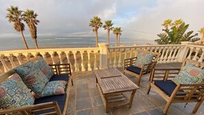Une terrasse dotée de mobilier en bois, d’un sol en pierre et offrant une vue sur l’océan.